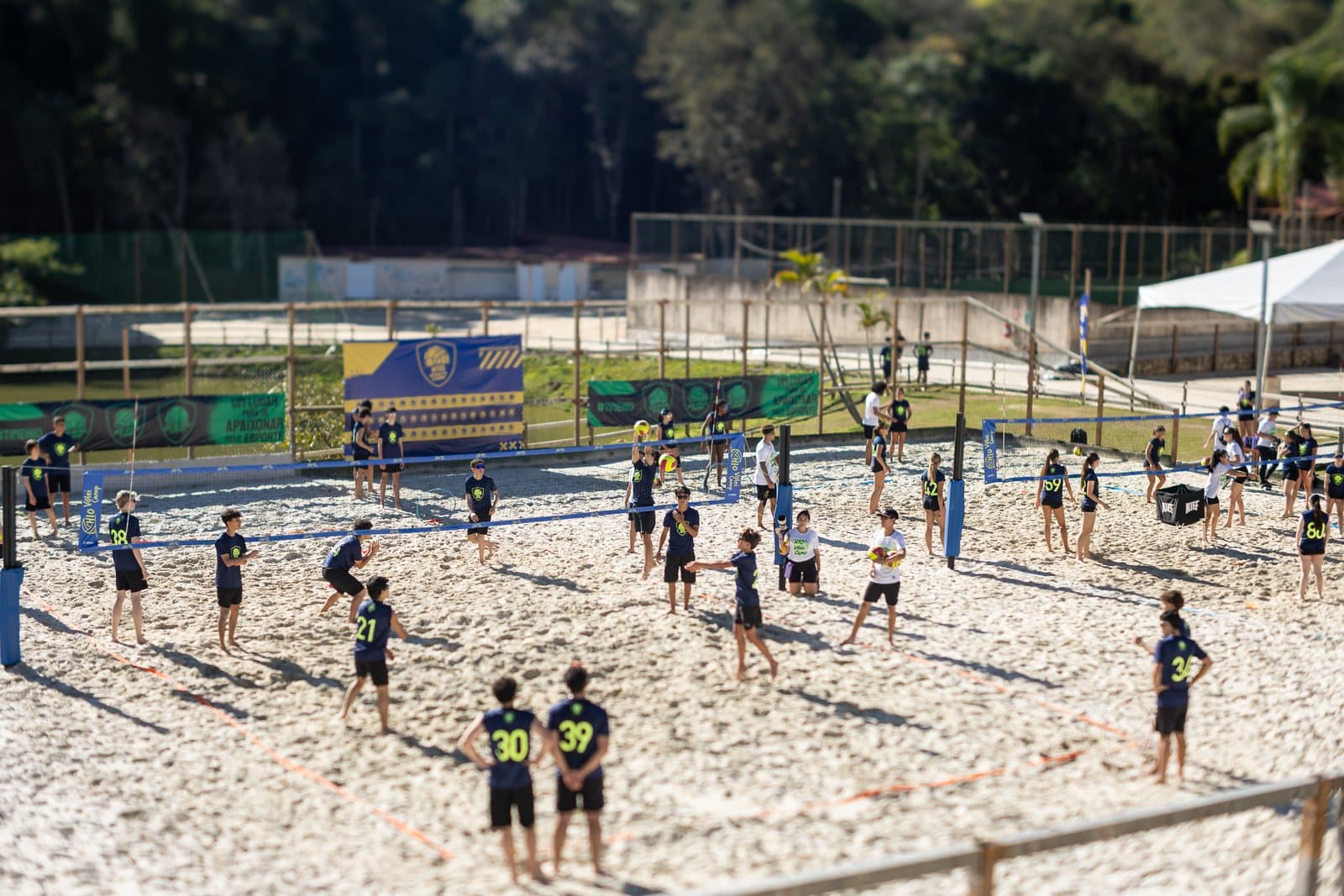 Arena de volei de praia com varias quadras de areia e acampantes jogando