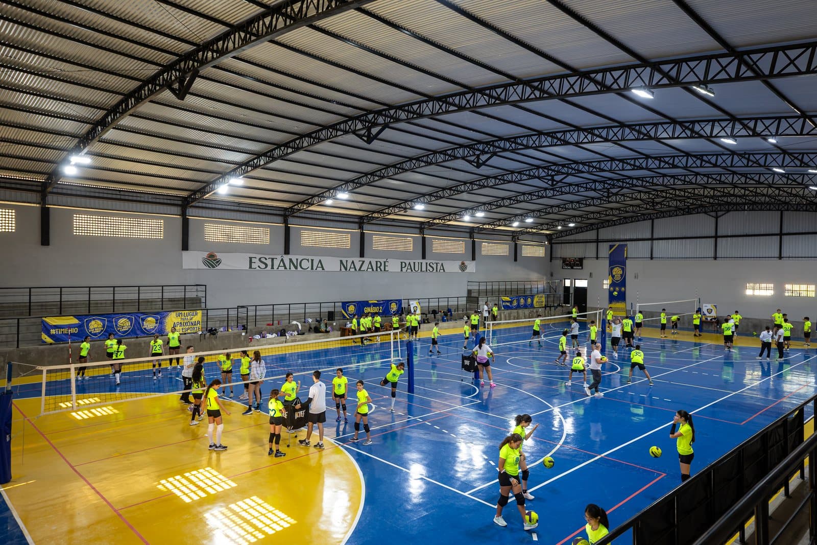 Ginasio coberto da Estancia com quatro quadras montadas e a turma de colete limao treinando