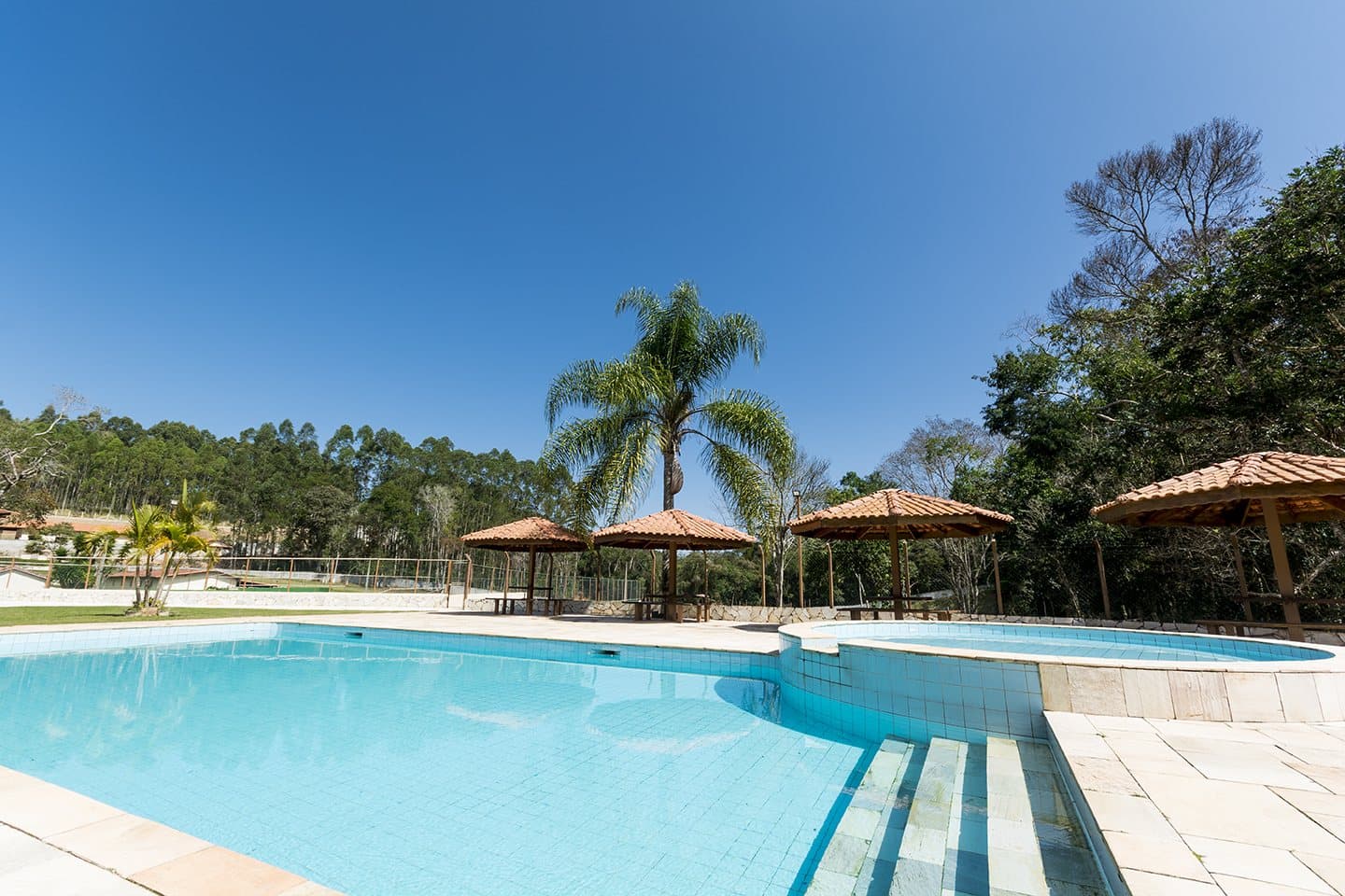 Piscina descoberta com quiosques de sape e coqueiros em volta