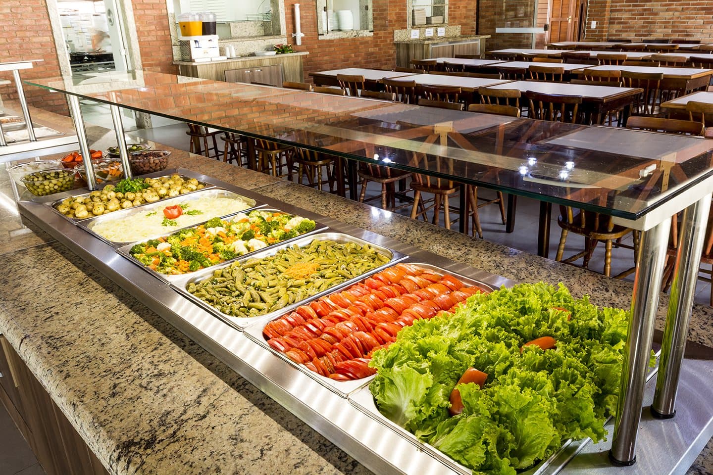 Buffet do refeitorio com saladas e pratos quentes, mesas do salao ao fundo